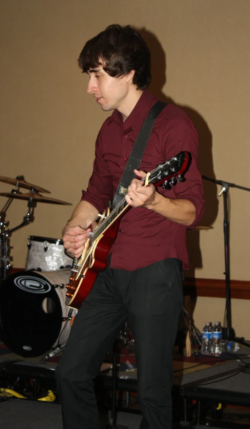 a man plays an electric guitar while another stands with his microphone nearby