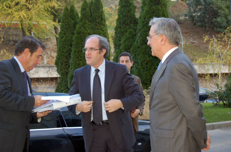 two men in suits are talking to a group of people