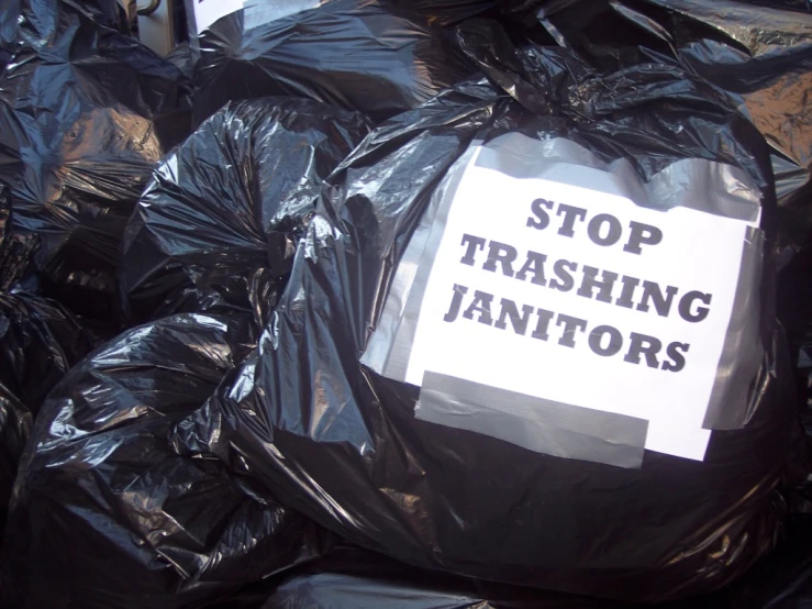 several black plastic bags filled with garbage and a sign saying stop trashing janitors