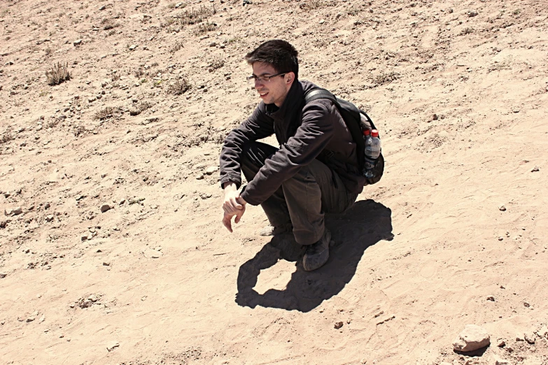 a man with a backpack crouching down in the sand