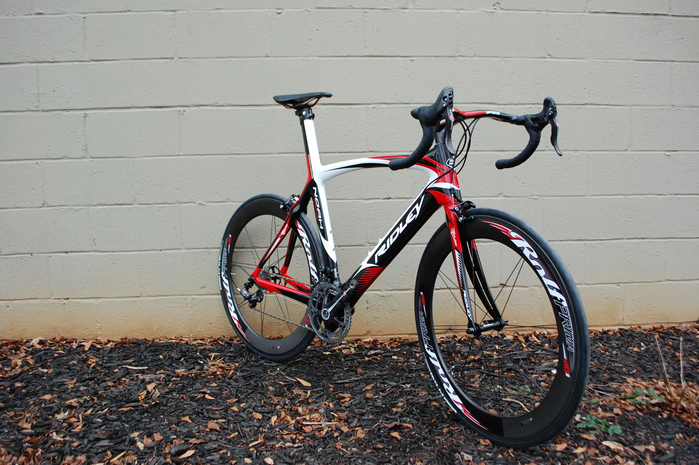 a white and red bike parked next to a brick wall