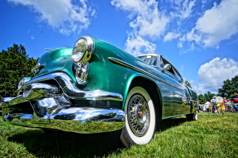 a vintage green car sitting in the grass near other cars