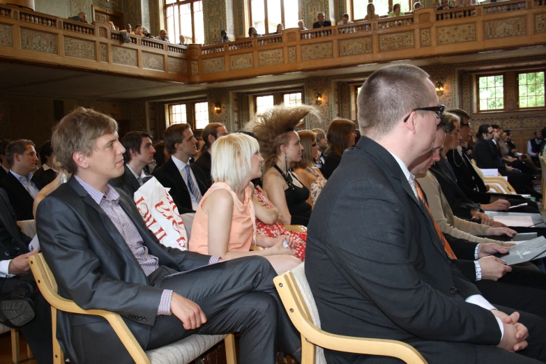 several people in suits seated in chairs in a hall