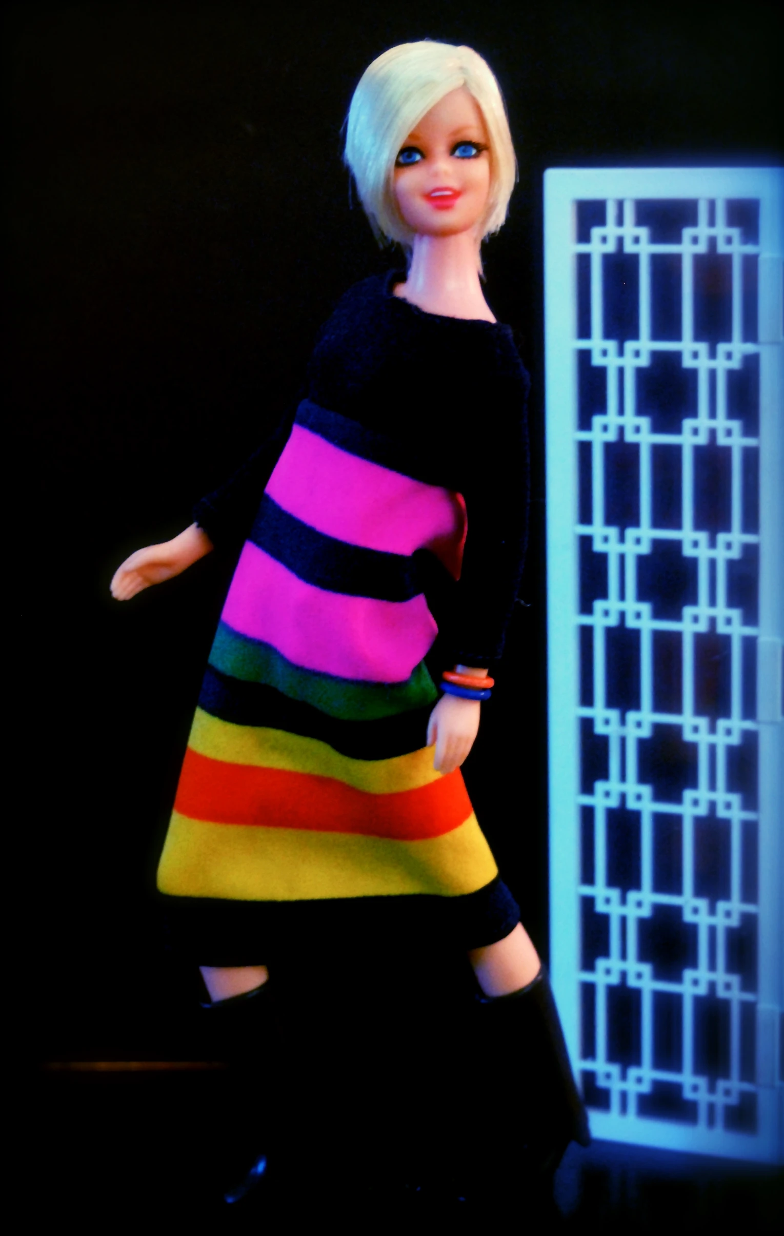 a barbie doll dressed in rainbows standing in front of a white door