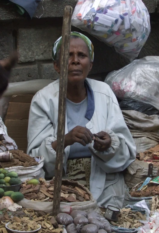 the woman in the white jacket is sitting next to some produce