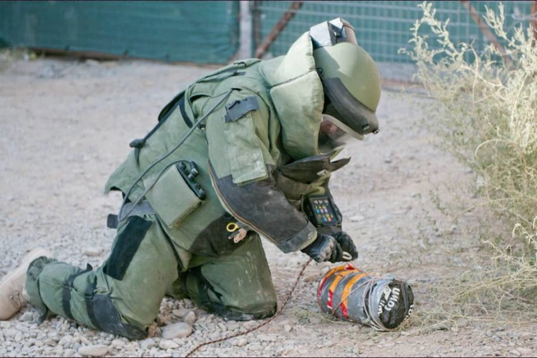 a man in military gear wearing an oxygen suit picking up a can of soda