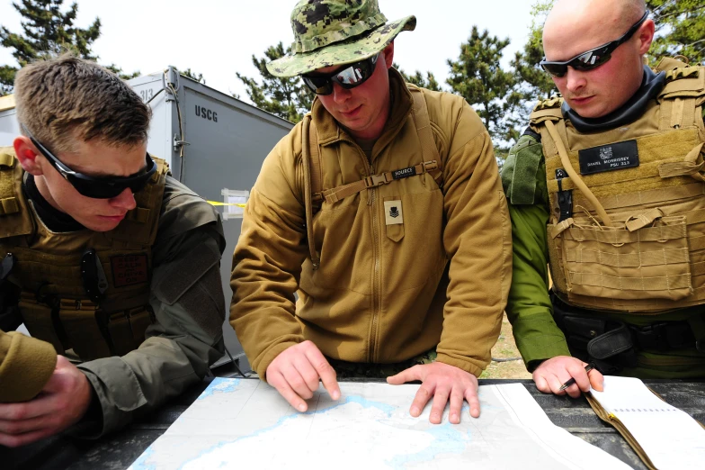 three men in military gear look at a map