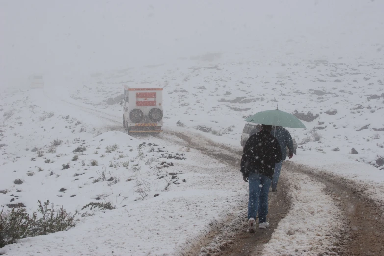 the man walks down a road in snow with an umbrella