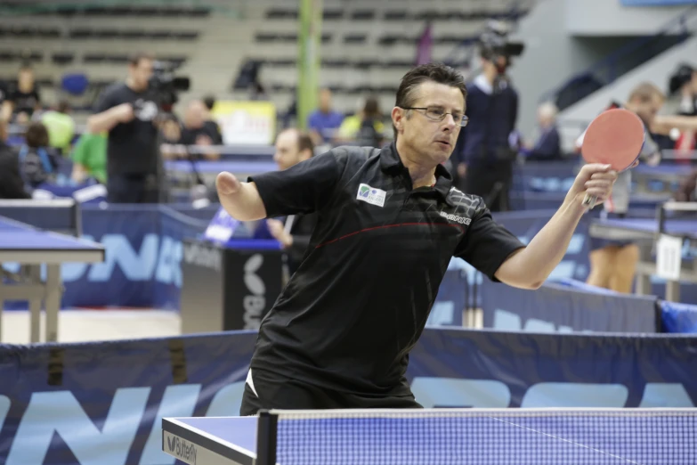 a man standing next to a ping pong net holding a red paddle