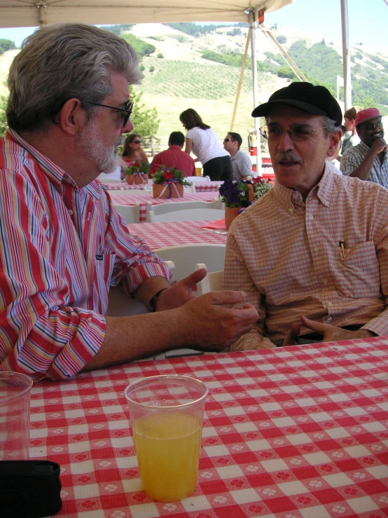 two men are sitting at a picnic table, having conversation