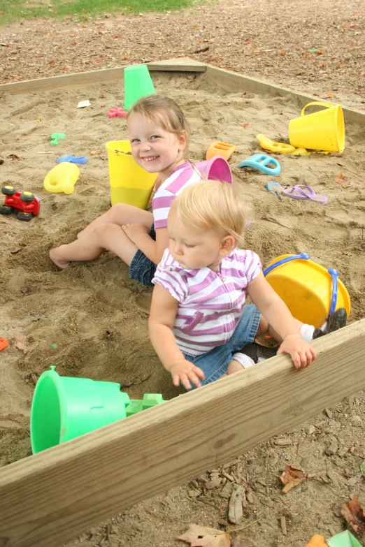 a couple of little girls playing with sand in a park