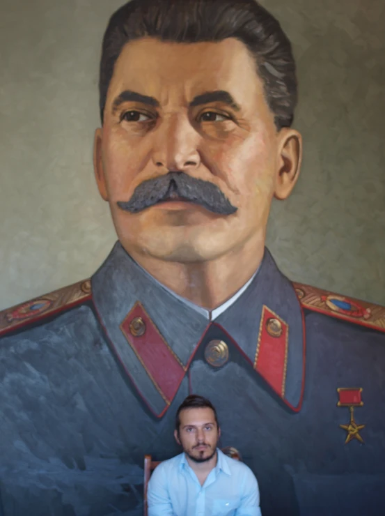 the man is sitting in front of the portrait of stalin