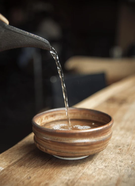 someone pours water in a bowl sitting on a wooden table