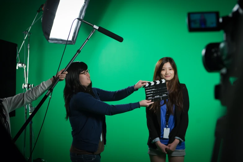 two women are taking pictures in front of a green screen