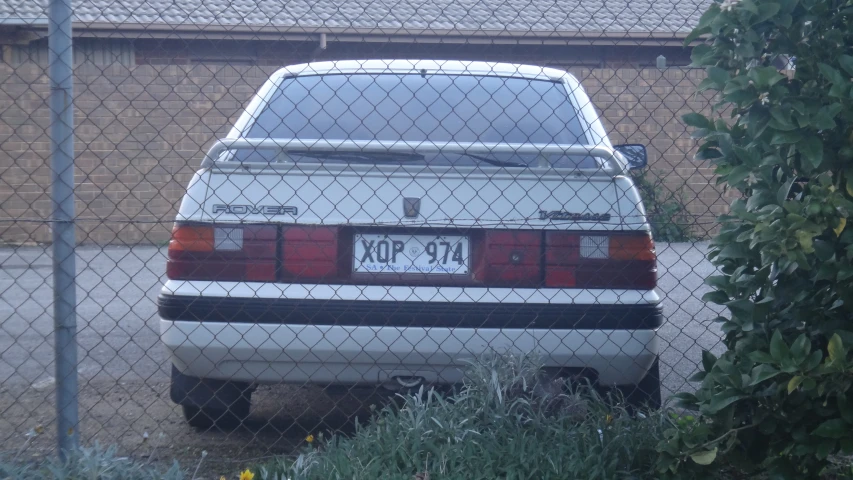 a white car parked behind a chain link fence