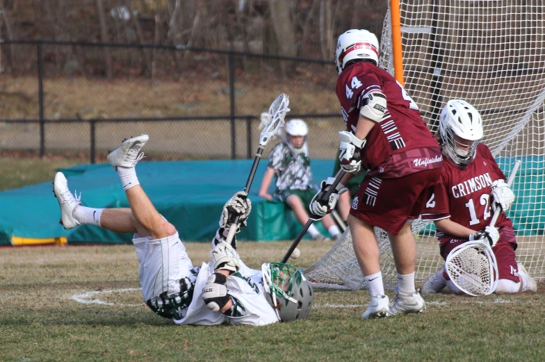 three lacrosse players in maroon jerseys, white helmets and white socks play a game