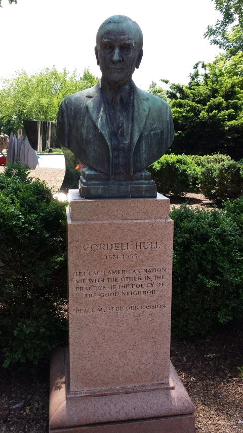 the bust of a man in front of a shrubbery area