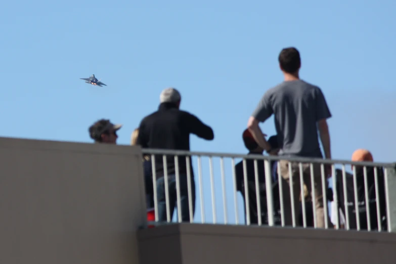 people are standing on the balcony and watching an airplane