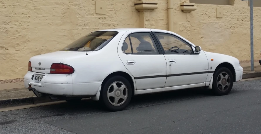 an almost white compact car sitting parked on the side of a street