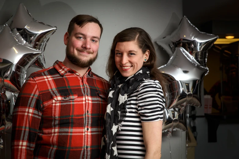 a young man and woman standing beside one another in front of balloons