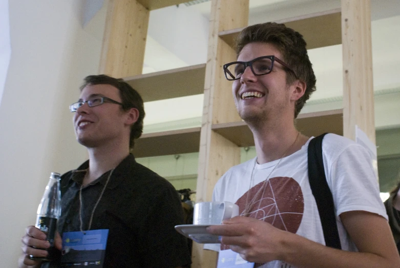 two guys standing up in a room and one holding a plate