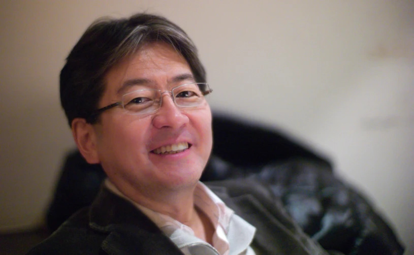 an asian man with glasses and a grey blazer smiling