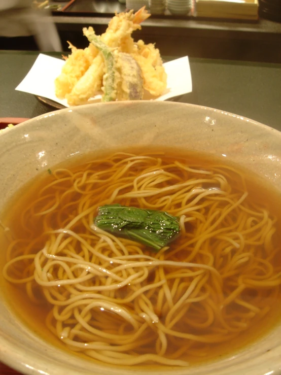 a bowl with noodles and greens on it next to some rolls