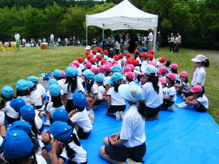 a man sits on the ground with a group of children who are wearing hats