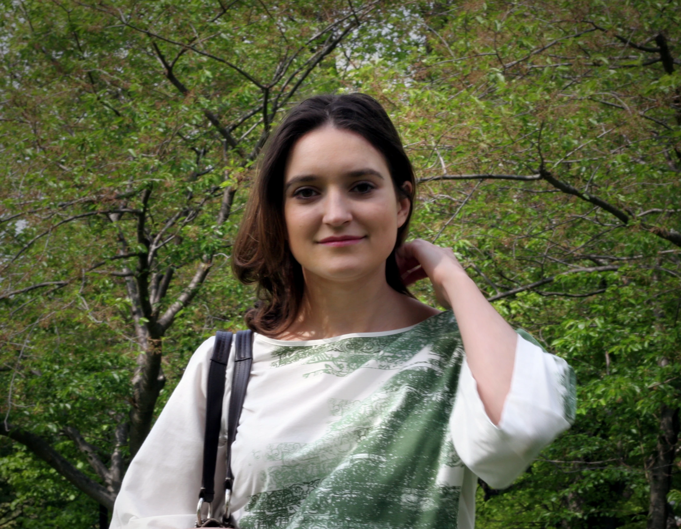 a young woman poses with a camera in front of some trees