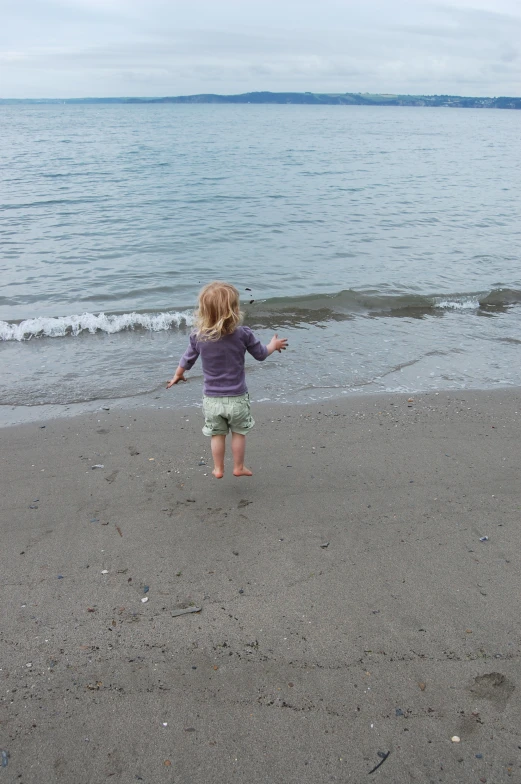 a toddler stands in front of the water as the waves come in