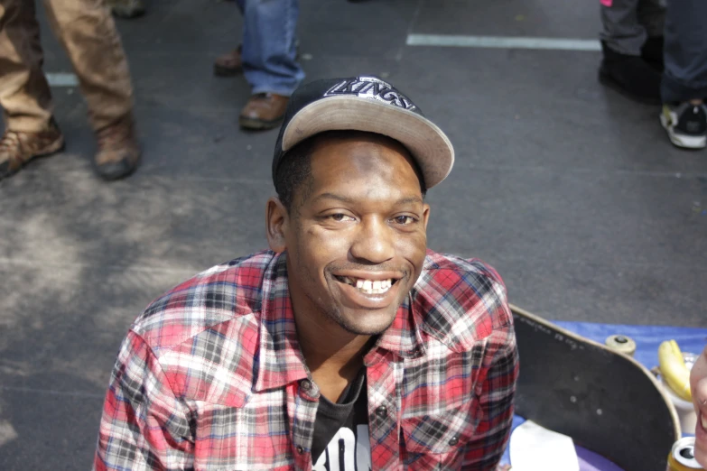 an african american man in a hat sitting by his skateboard