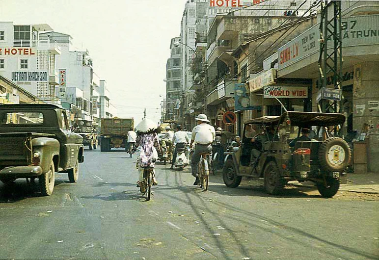 several people ride bicycles and motorcycles down a busy street