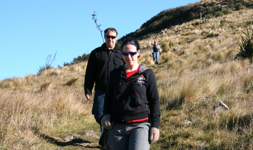 two people walking up a grassy hill by the side of a hillside