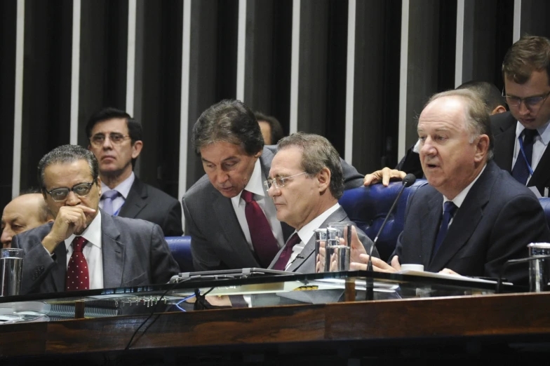 two men sitting at a microphone with one man holding a pen in his hand