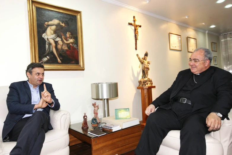 two men sitting on couches one wearing a suit and the other in business