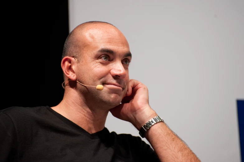 a bald man in a black shirt talking on his cellphone