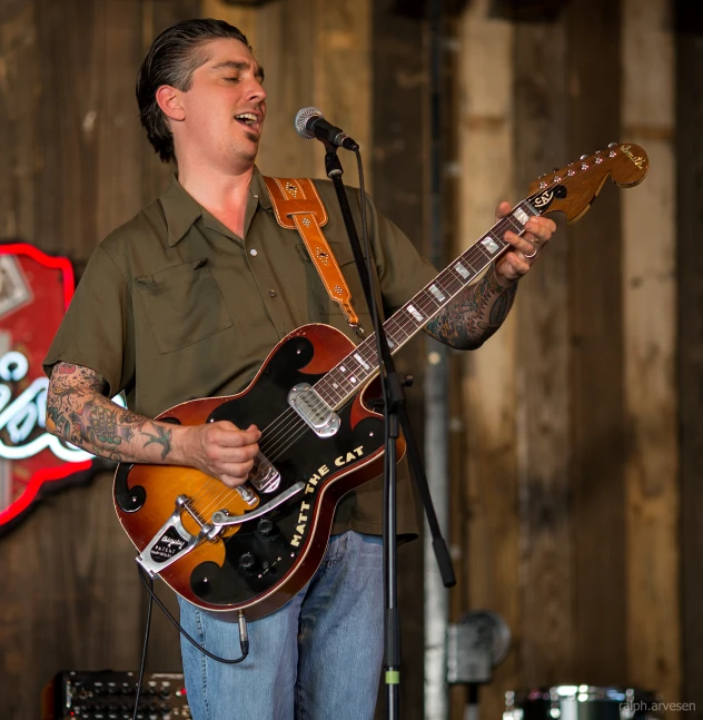 man with tattoo on playing guitar in front of a microphone