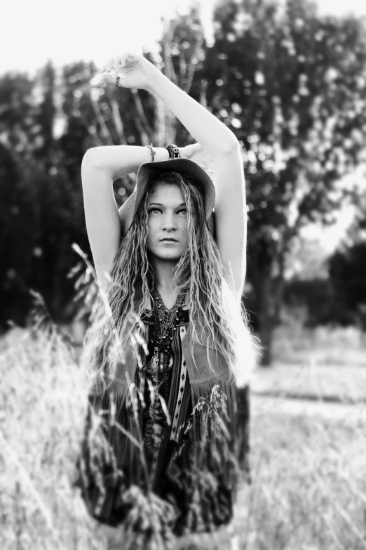 a woman stands in the tall grass with her hat on her head