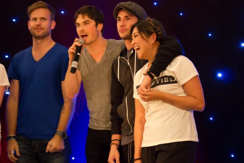 six men standing and holding a microphone together