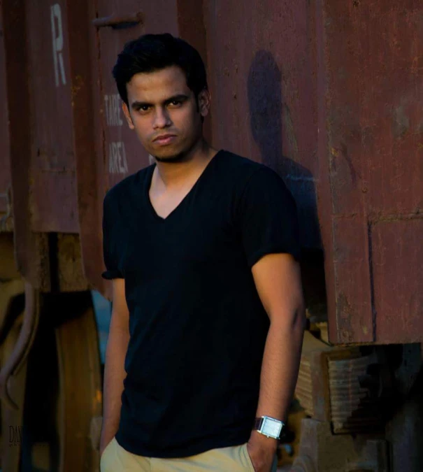 a man poses for a pograph while posing in front of some old cargo