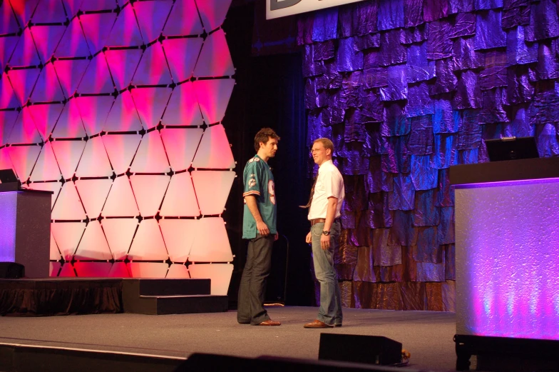 two men standing on a stage with one holding a cellphone