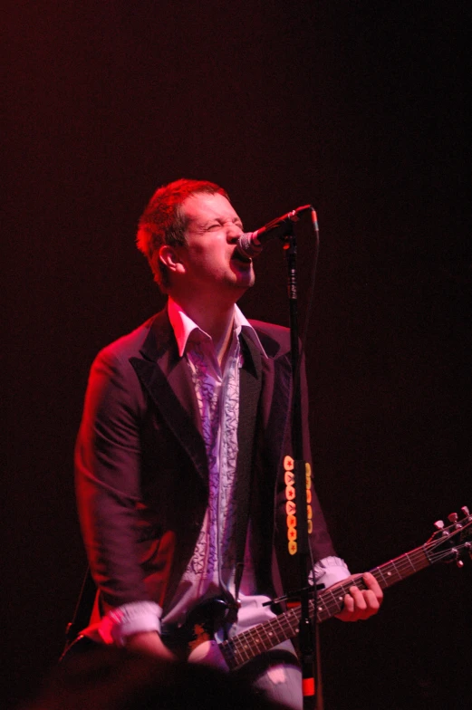 a person in a suit singing into a microphone and holding a guitar