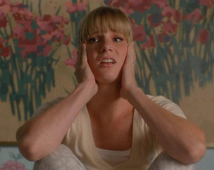 a woman sits in a room holding her head and touching her forehead