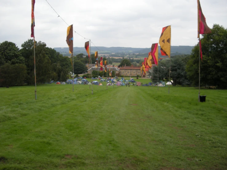 several flags on poles near a field with tents