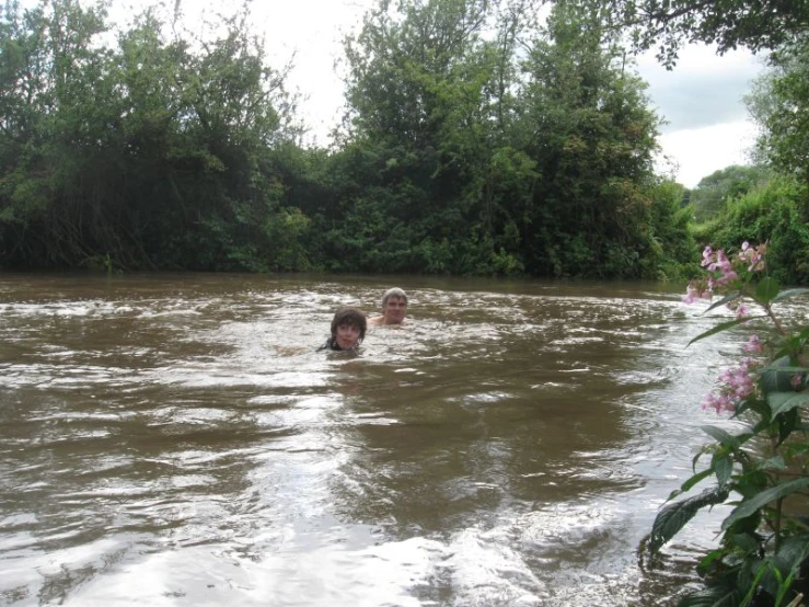 two boys swimming in the water near some trees