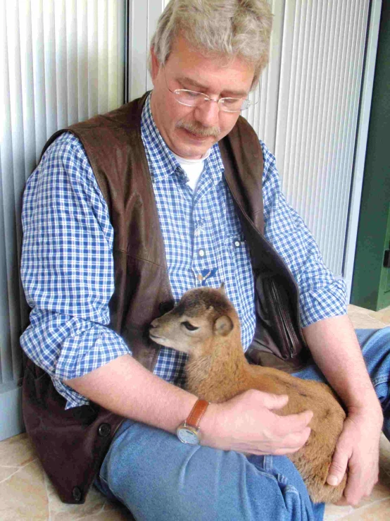 man in blue and white shirt sitting on the ground with small brown animal