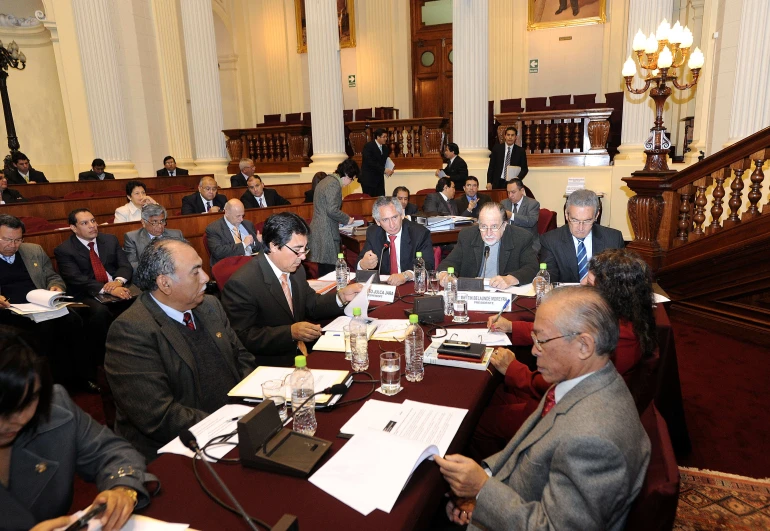 a group of people are sitting at a long table with paperwork