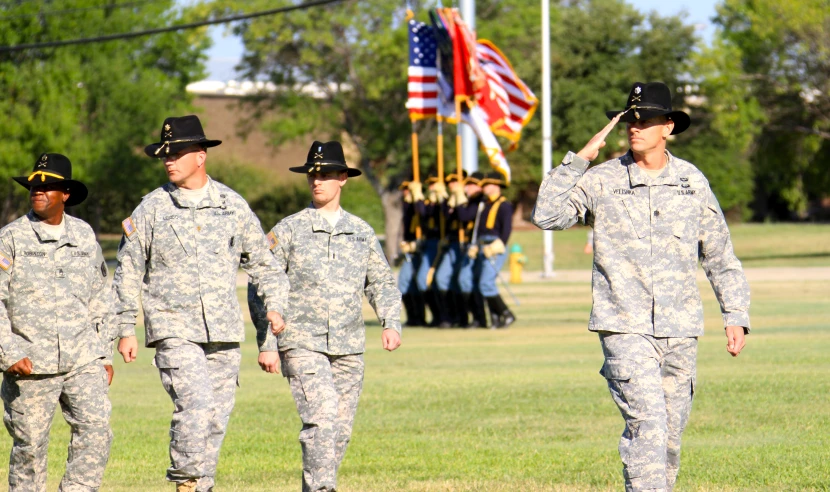 four uniformed men in uniforms walking by a flag