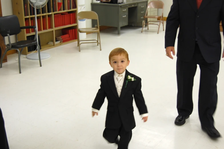 a little boy in a suit walking across a room