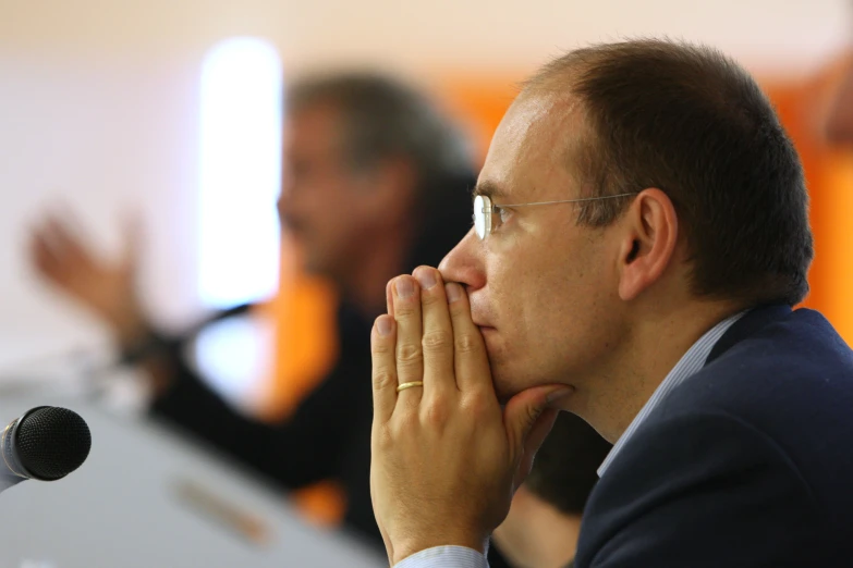 a man in a business suit is holding his hands over his face while a woman in the background looks on